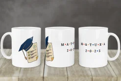 Biały kubek z nadrukiem czapki absolwenta i napisem Matura 2025 na tle drewnianego blatu